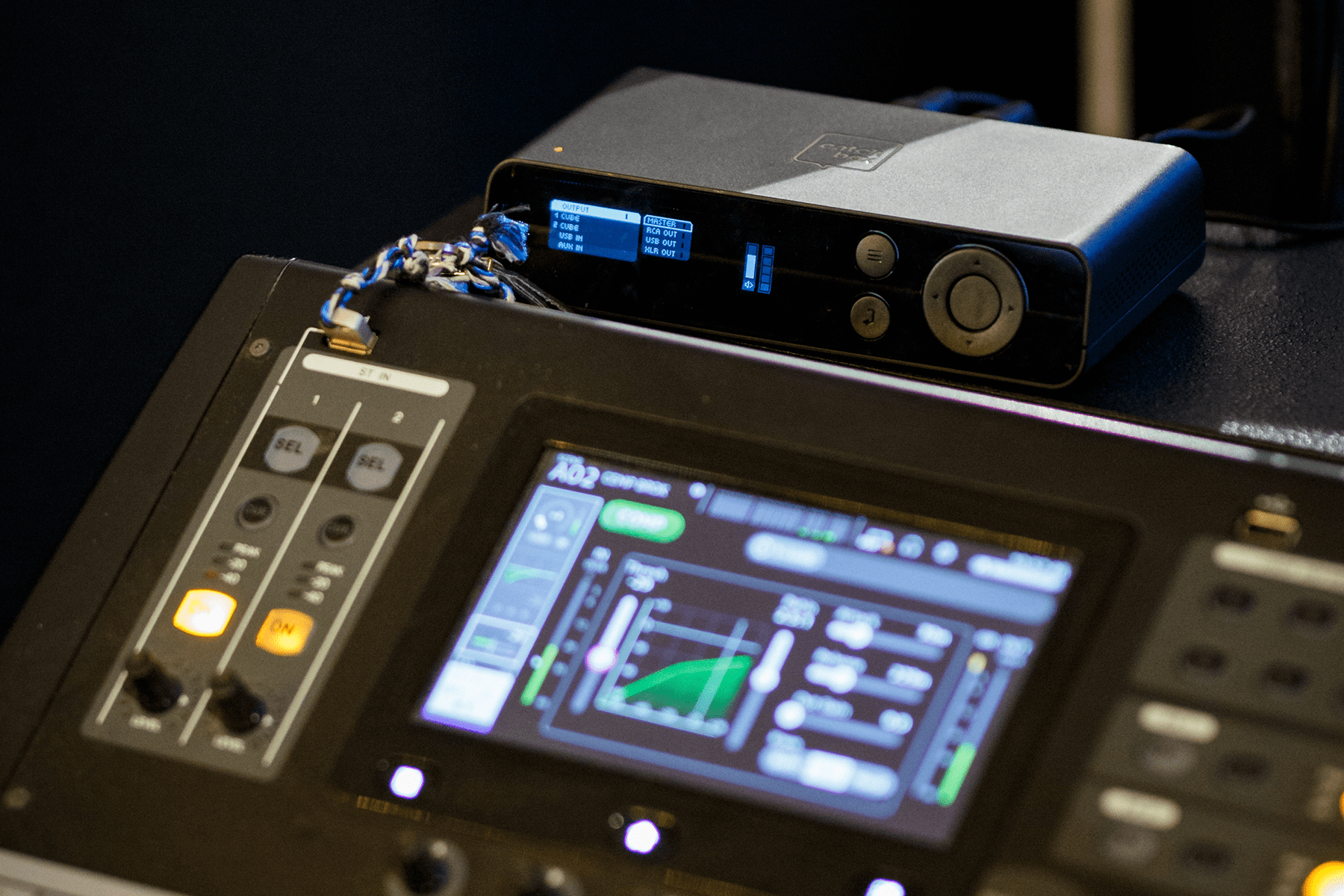 Close-up of a Catchbox Hub DSP placed on an audio mixing console, displaying input and output settings on its screen for audio management.