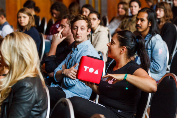 Audience member holding a red Catchbox Cube microphone customized with the TOA logo, engaging in a discussion during a session, demonstrating how high-quality audio can enhance hybrid events and make them engaging for all attendees.